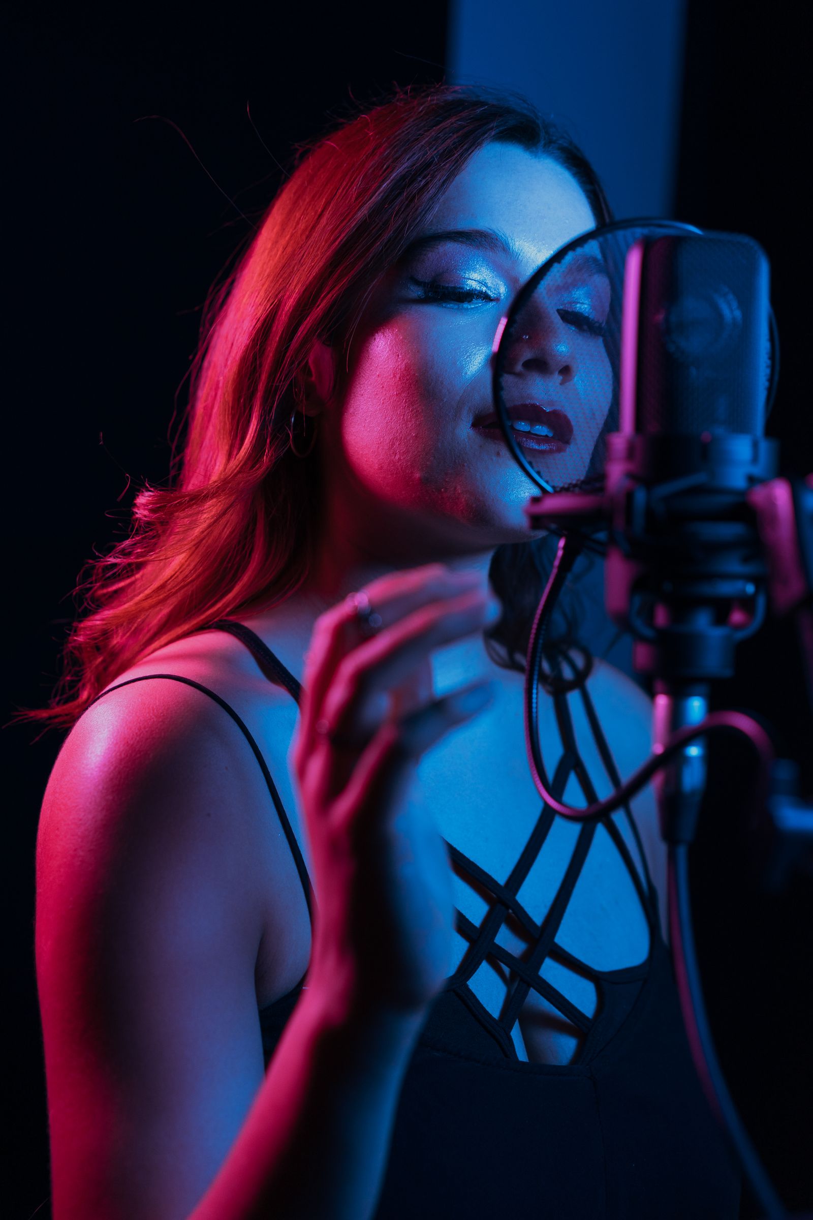 A singer at a condenser microphone, lit in pink and blue neon